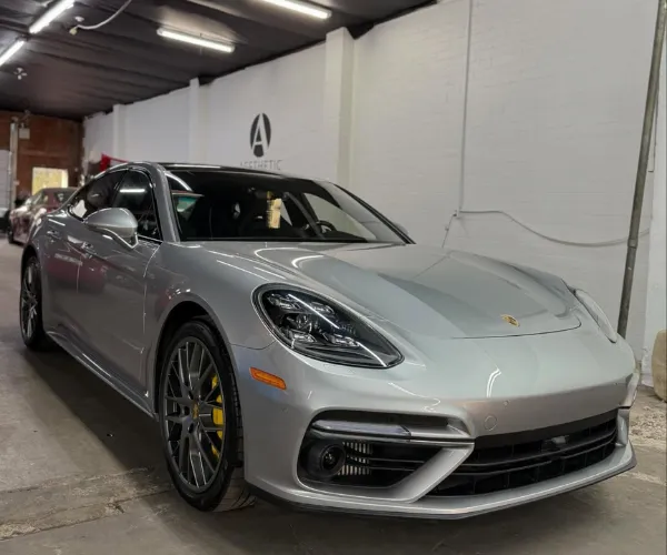 A side profile view of the dark grey sedan, highlighting the clean, uniform application of dark window tint across the side windows under professional workshop lighting.
