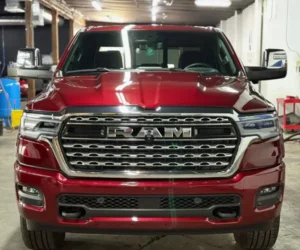 view of a metallic cherry red RAM pickup truck parked inside a detailing bay, showcasing a glossy finish and overhead light reflections across the hood and body panels, as seen in paint correction