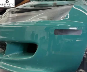 clear paint protection film being meticulously applied to the front bumper of a teal sports car