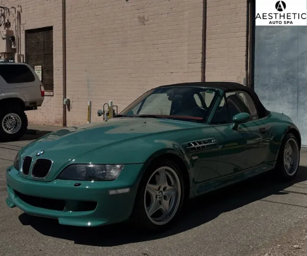 clear paint protection film being meticulously applied to the front bumper of a teal sports car